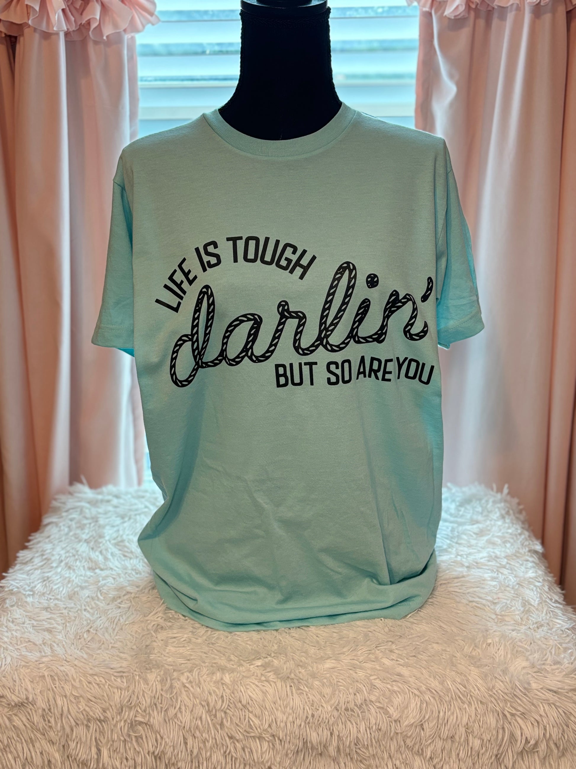 Light blue heat press t-shirt with motivational quote on a textured surface- Life is tough darlin but so are you