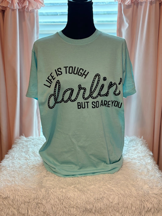 Light blue heat press t-shirt with motivational quote on a textured surface- Life is tough darlin but so are you