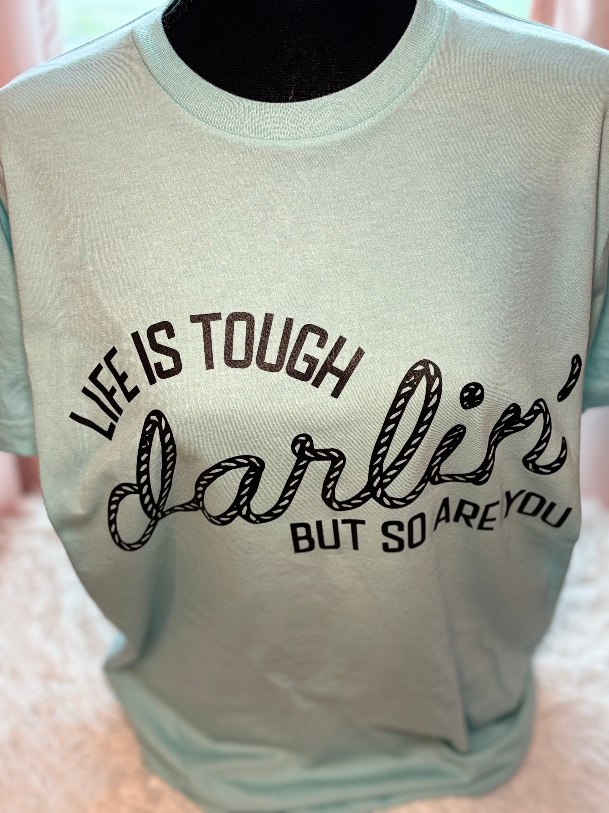 Light blue heat press t-shirt with motivational quote on a textured surface- Life is tough darlin but so are you
