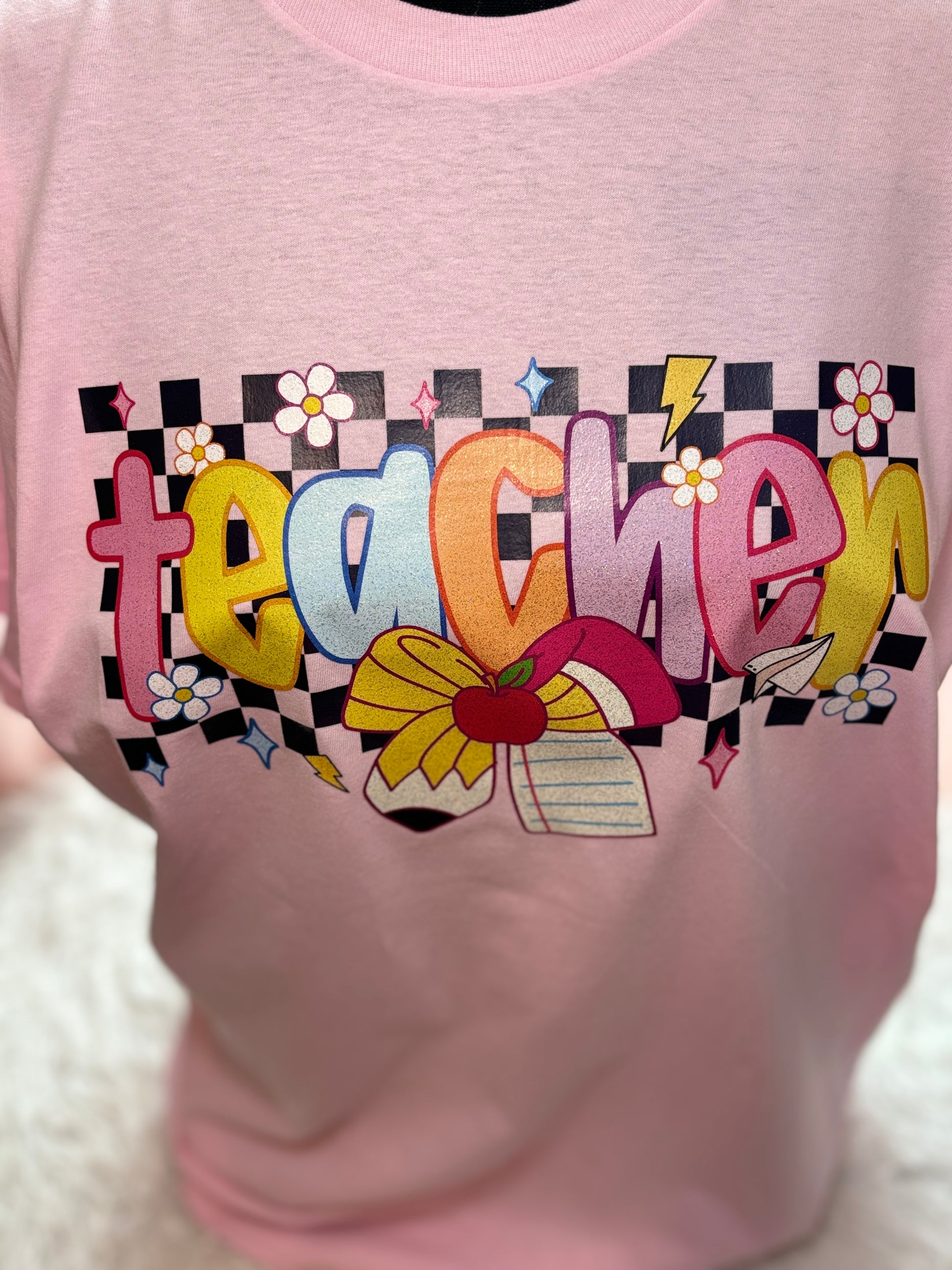 Pink heat press t-shirt with colorful 'teacher' design with checker background and pencil / paper bow