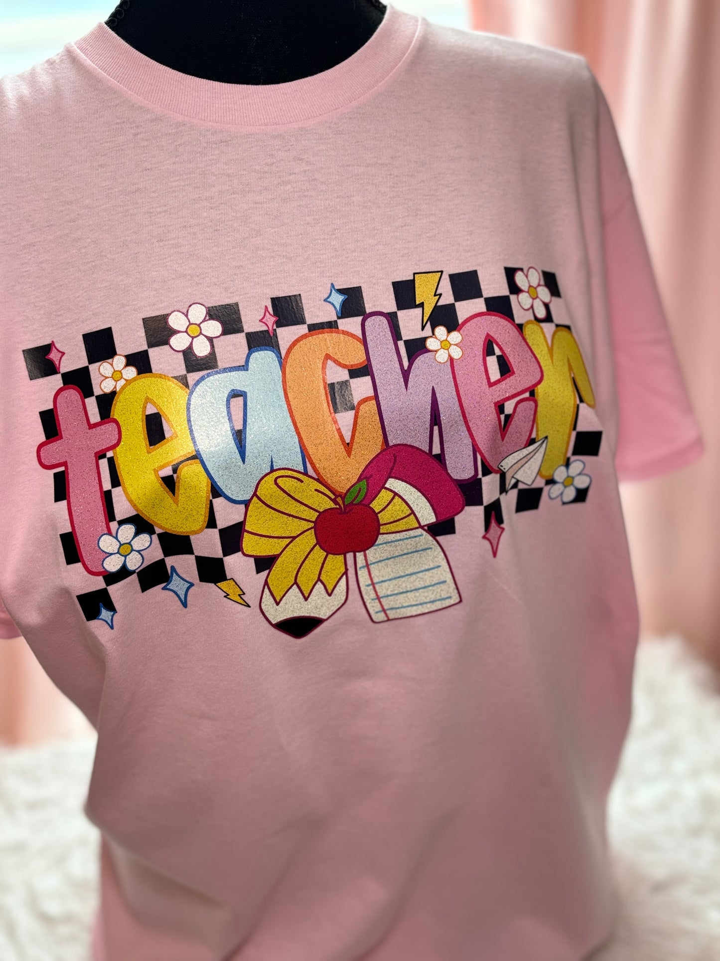 Pink heat press t-shirt with colorful 'teacher' design with checker background and pencil / paper bow
