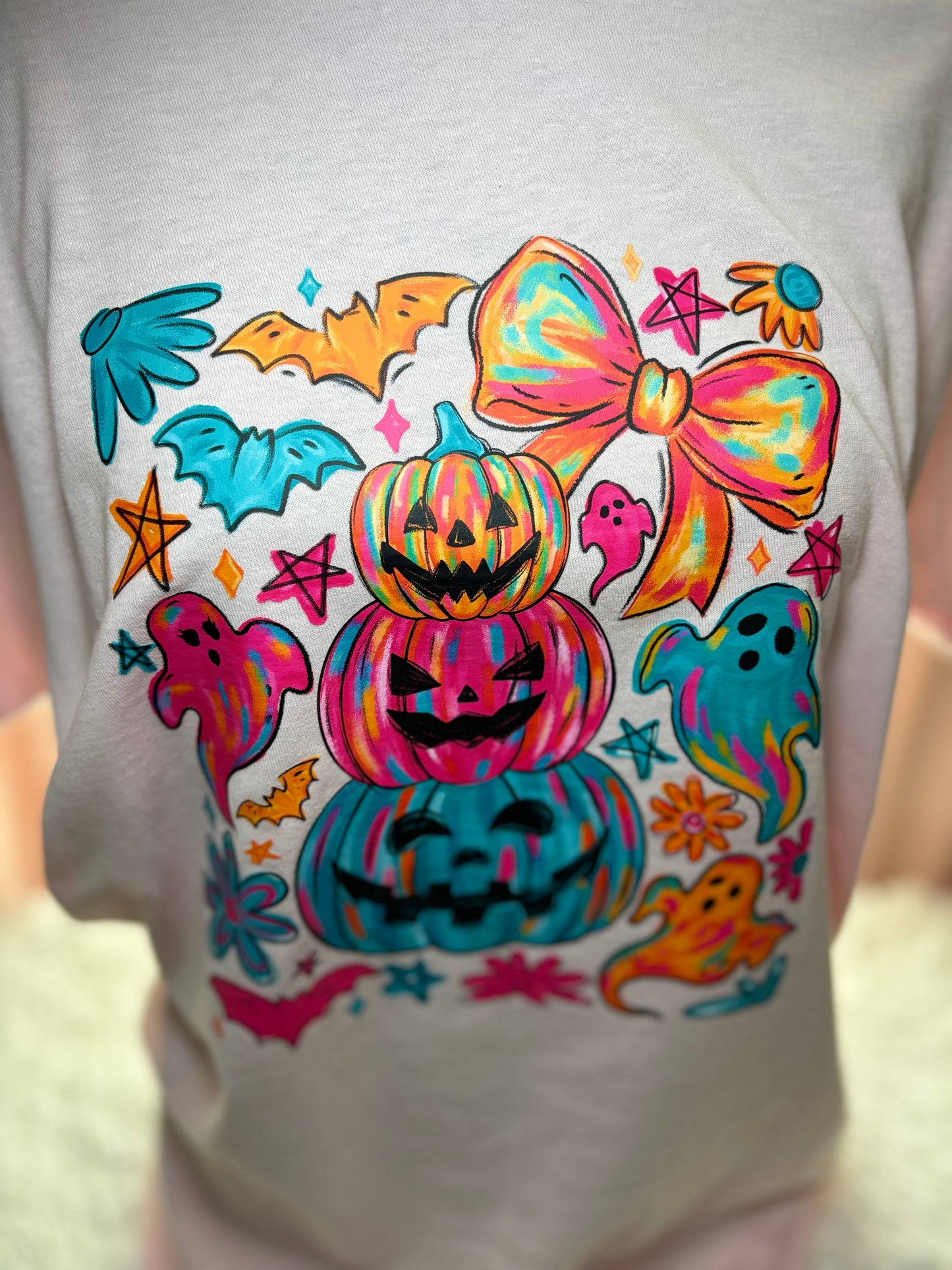 Colorful Halloween-themed heat press design on a pink shirt with pumpkins, ghosts, and bows.