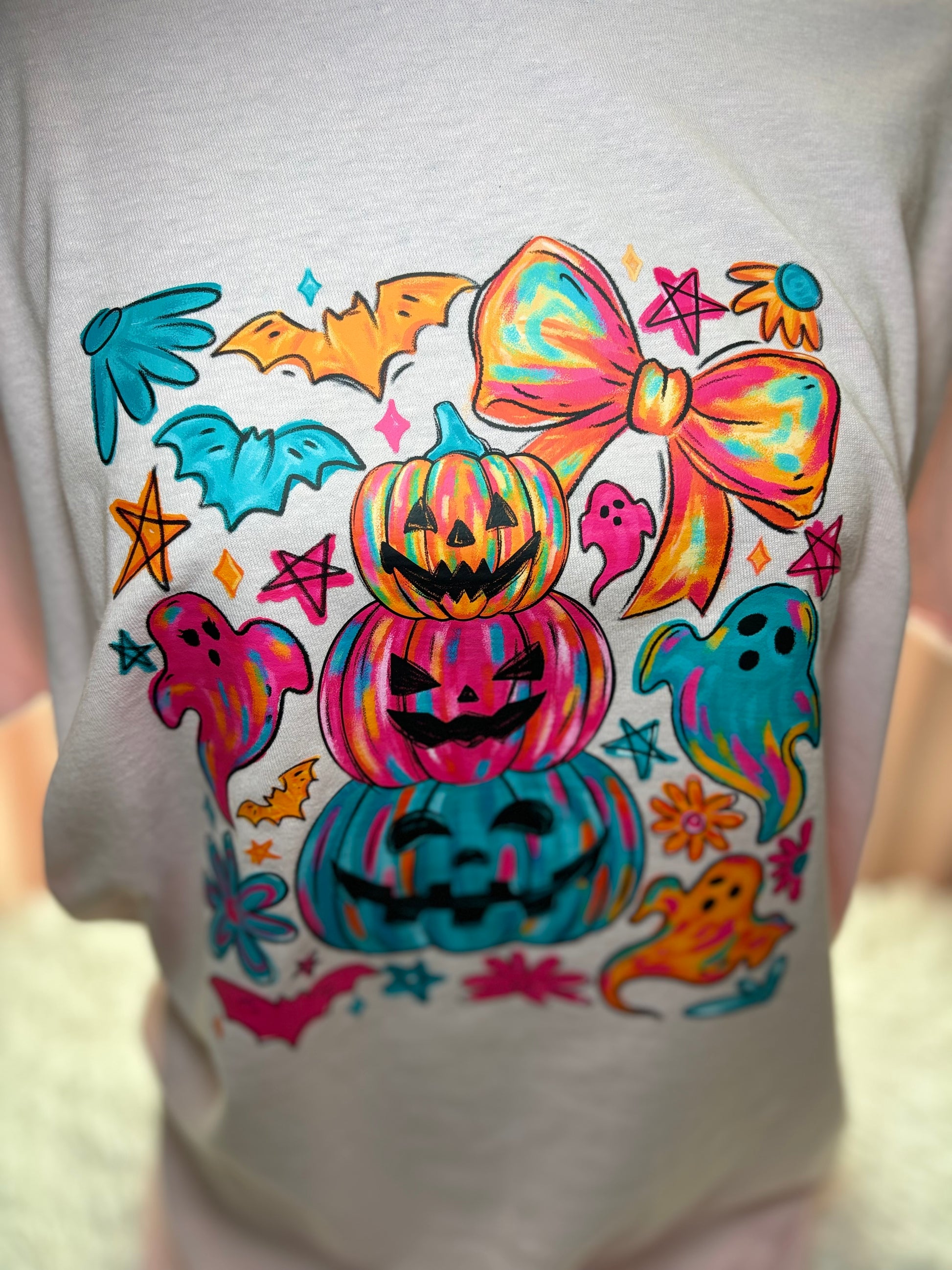 Colorful Halloween-themed heat press design on a pink shirt with pumpkins, ghosts, and bows.