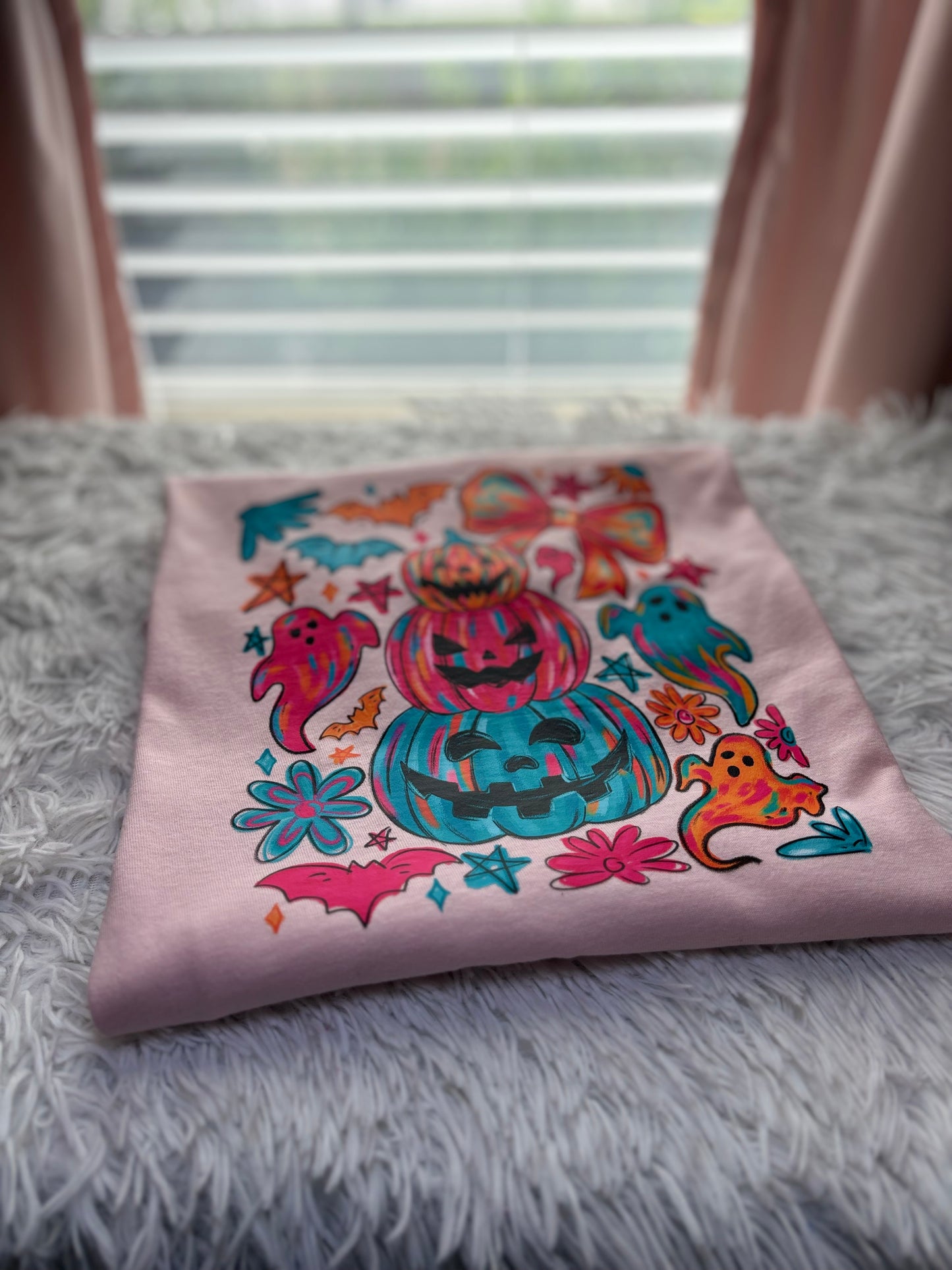 Colorful Halloween-themed heat press design on a pink shirt with pumpkins, ghosts, and bows.