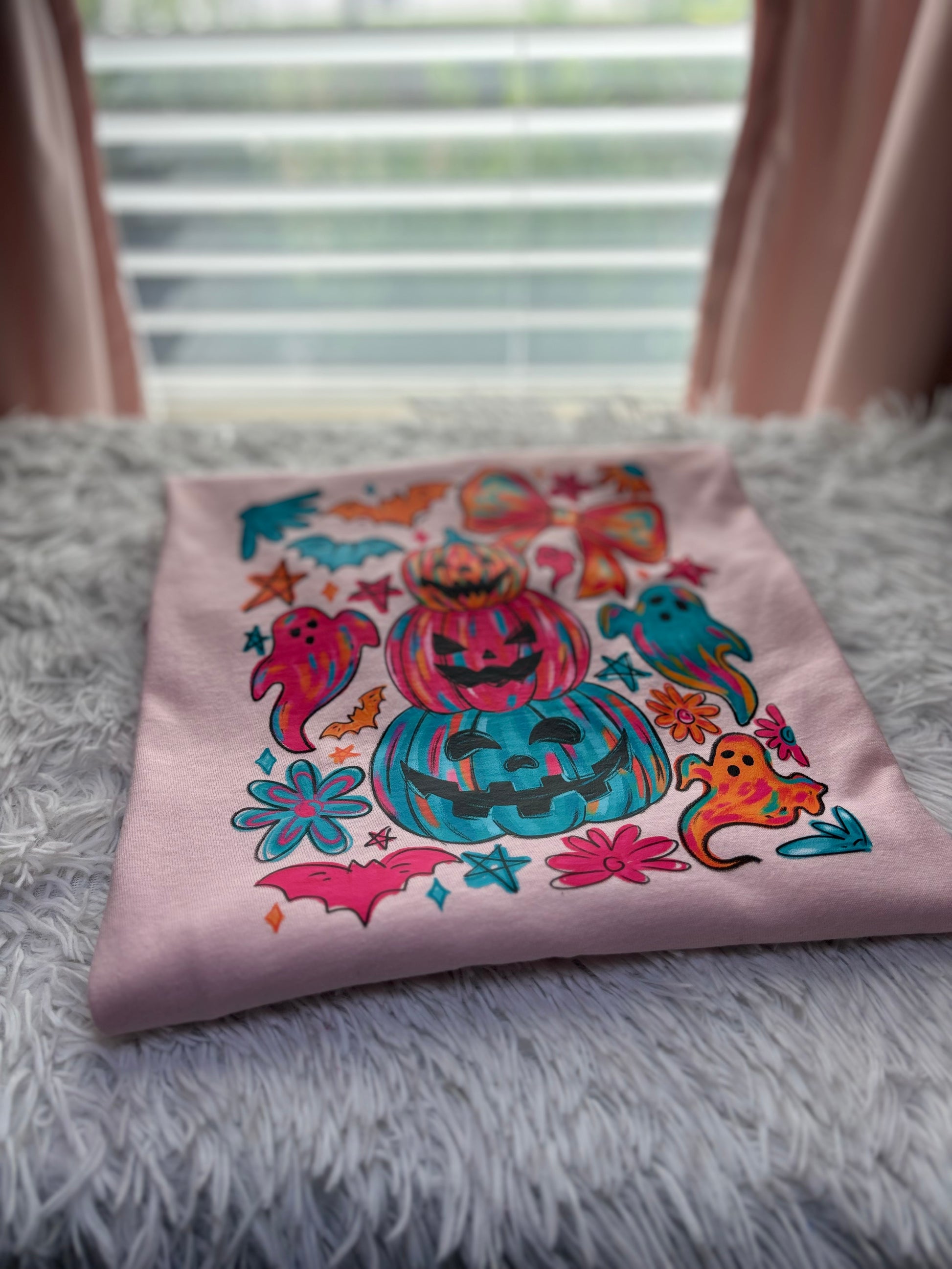 Colorful Halloween-themed heat press design on a pink shirt with pumpkins, ghosts, and bows.