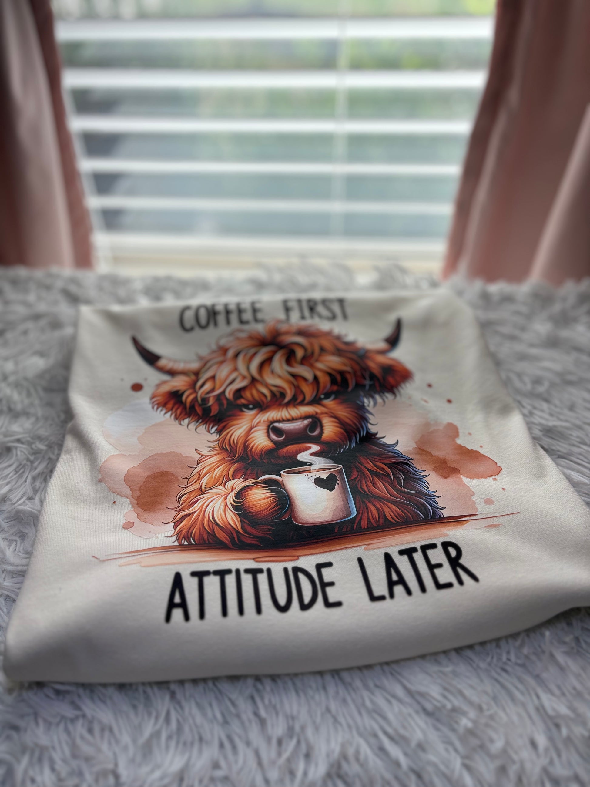 Beige heat press t-shirt with a Highland cow holding a coffee cup and text 'Coffee First, Attitude Later'