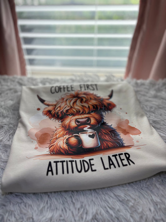 Beige heat press t-shirt with a Highland cow holding a coffee cup and text 'Coffee First, Attitude Later'