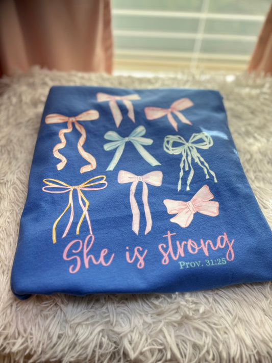 Blue heat press pocket t-shirt with colorful bows and 'She is strong' text on the back and bow on the front pocket