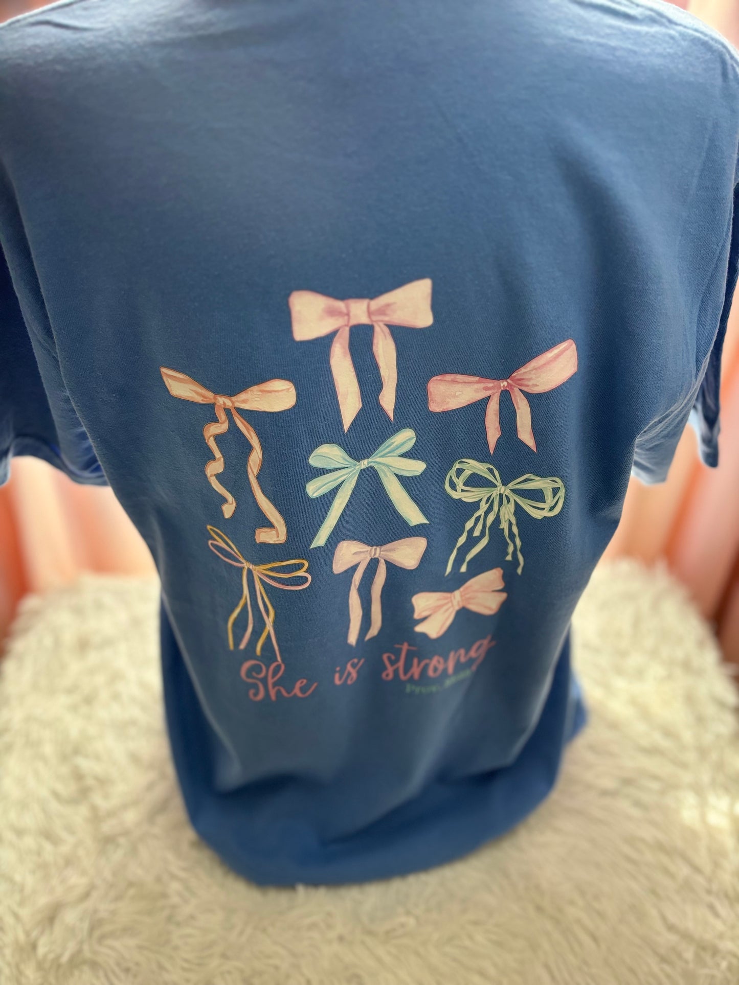 Blue heat press pocket t-shirt with colorful bows and 'She is strong' text on the back and bow on the front pocket