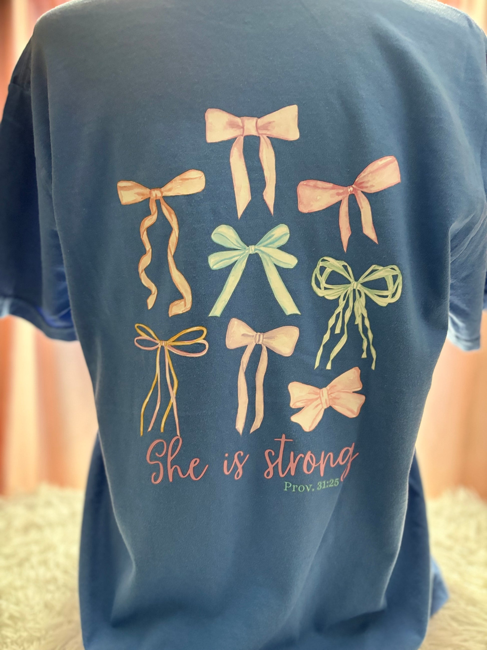Blue heat press pocket t-shirt with colorful bows and 'She is strong' text on the back and bow on the front pocket