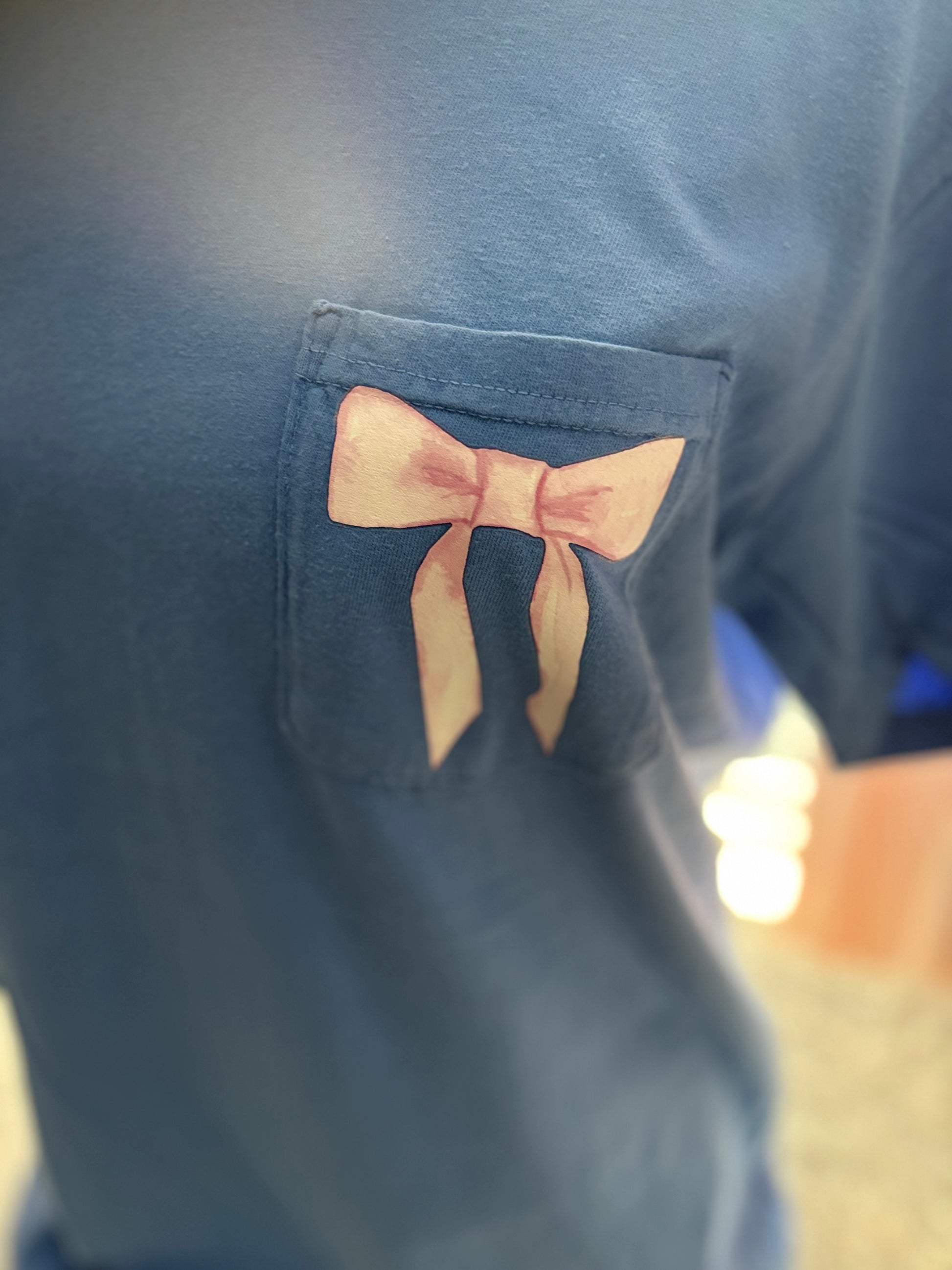 Blue heat press pocket t-shirt with colorful bows and 'She is strong' text on the back and bow on the front pocket
