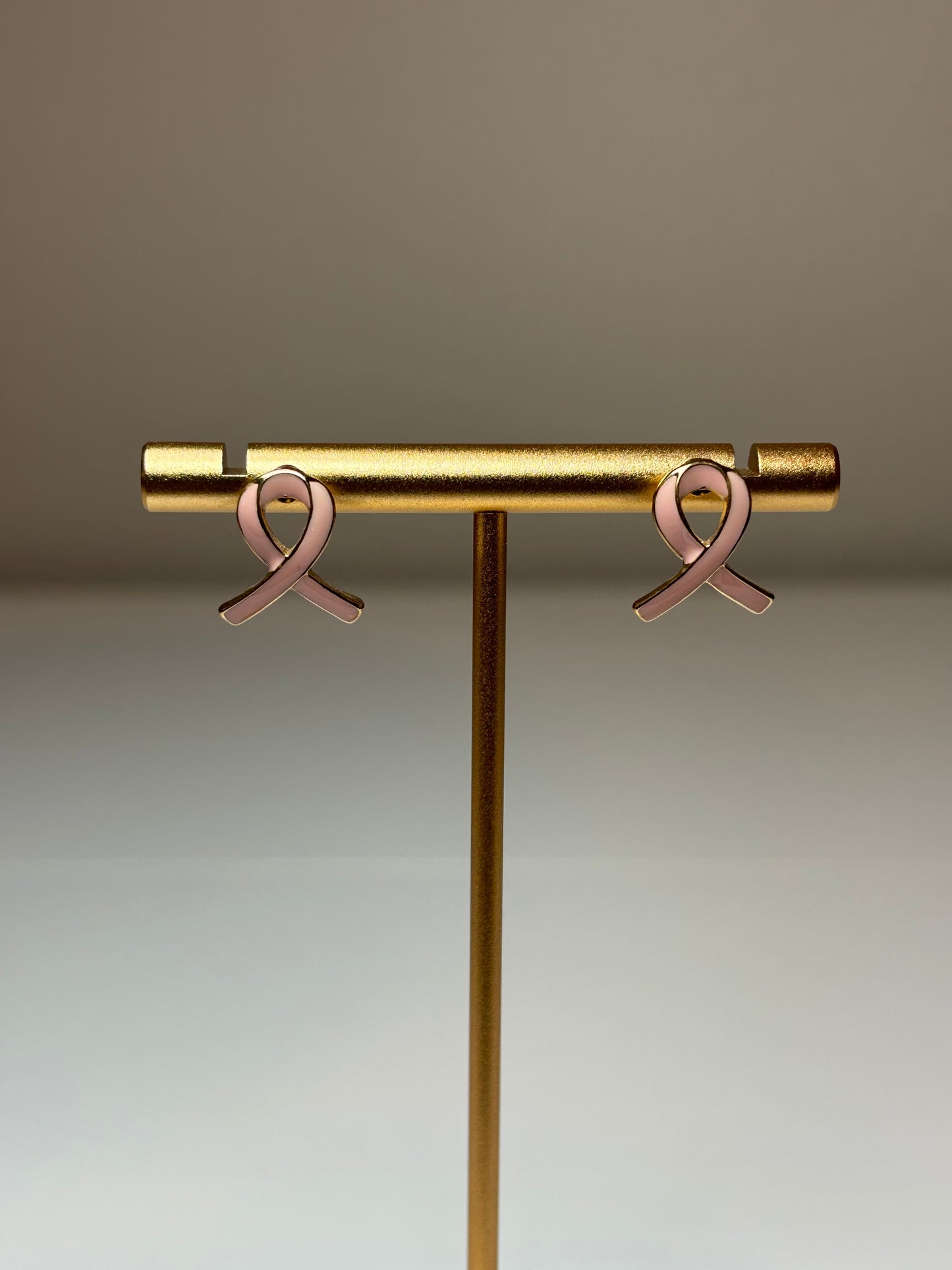 Pink ribbon earrings on a gold background