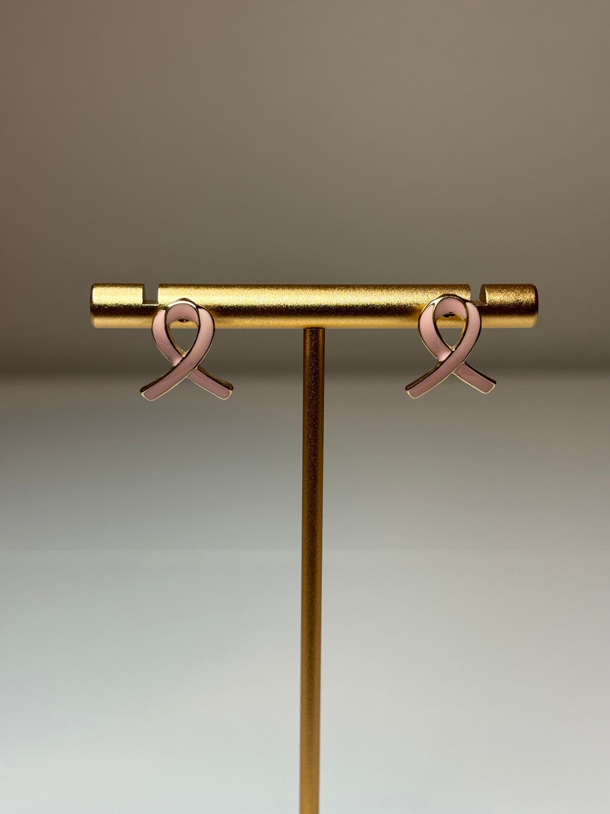Pink ribbon earrings on a gold background