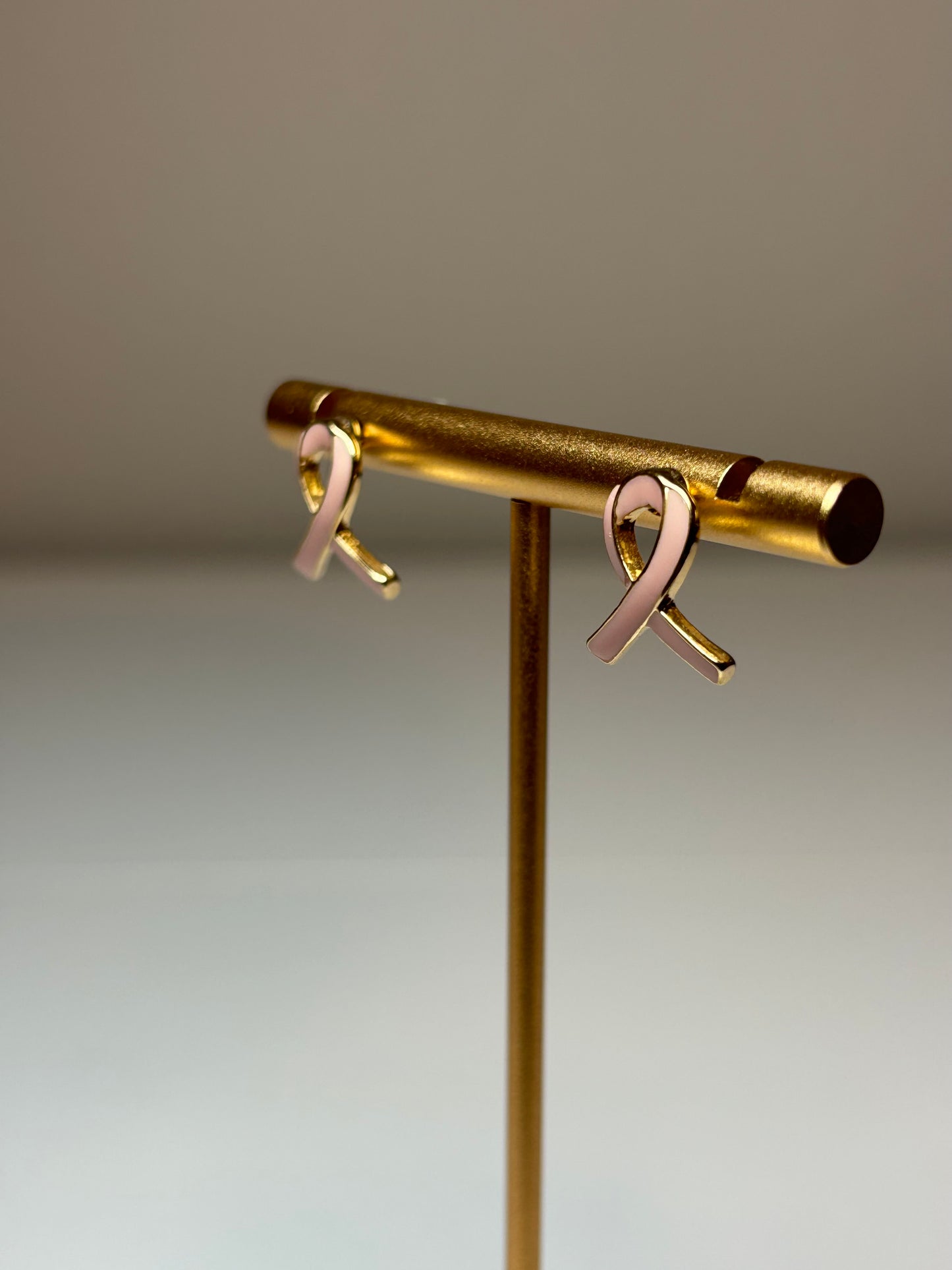 Pink ribbon earrings on a gold background