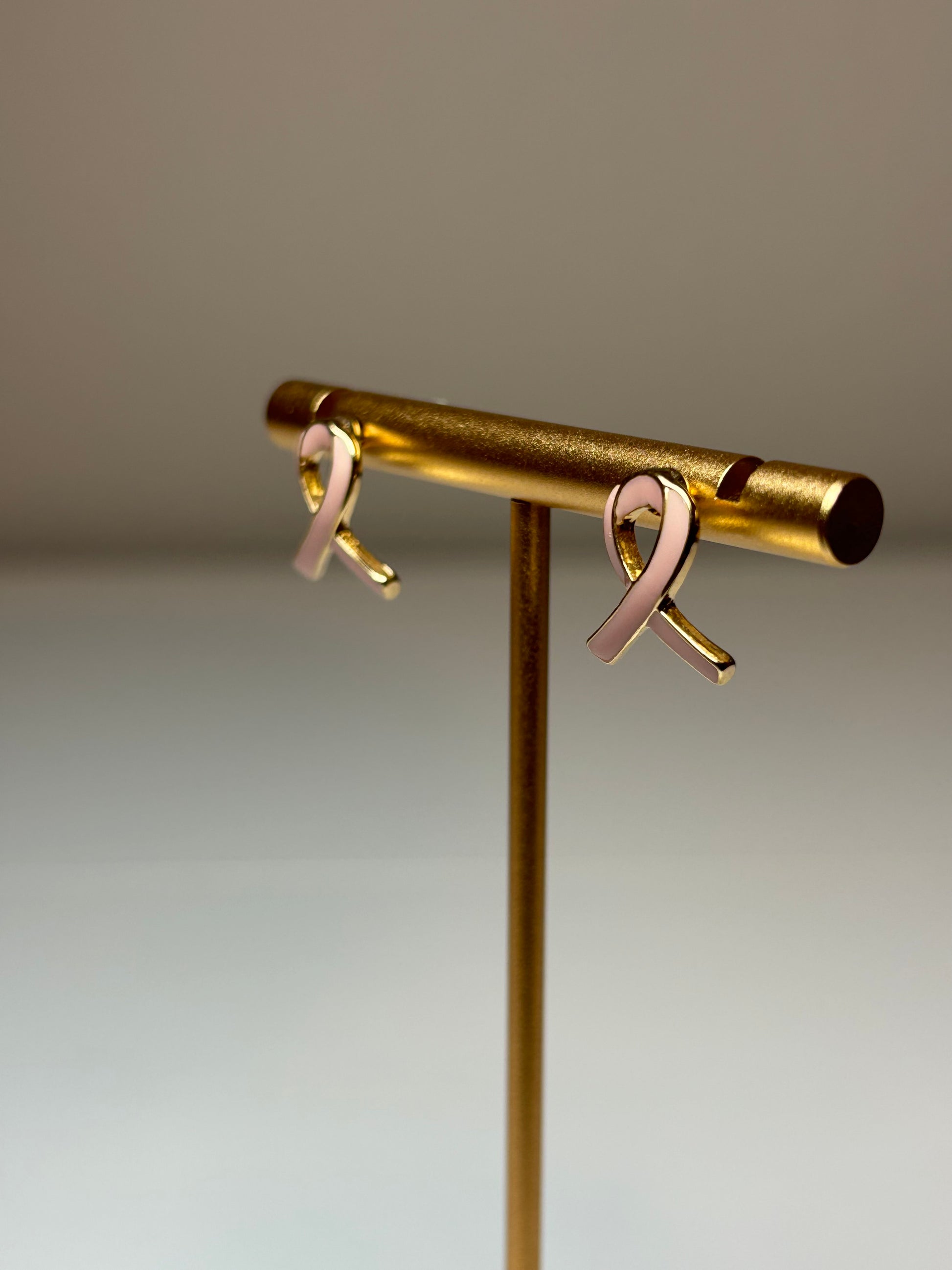 Pink ribbon earrings on a gold background
