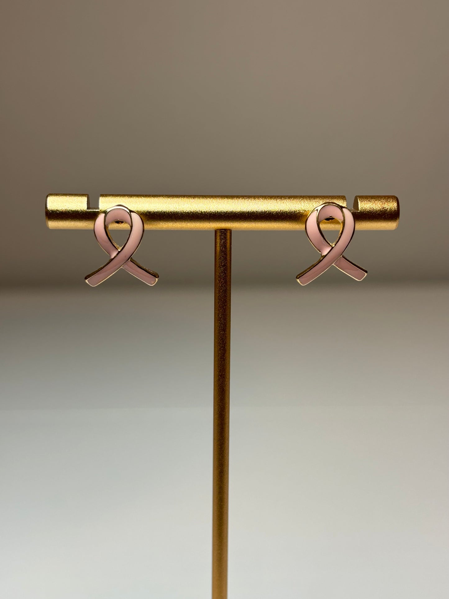 Pink ribbon earrings on a gold background
