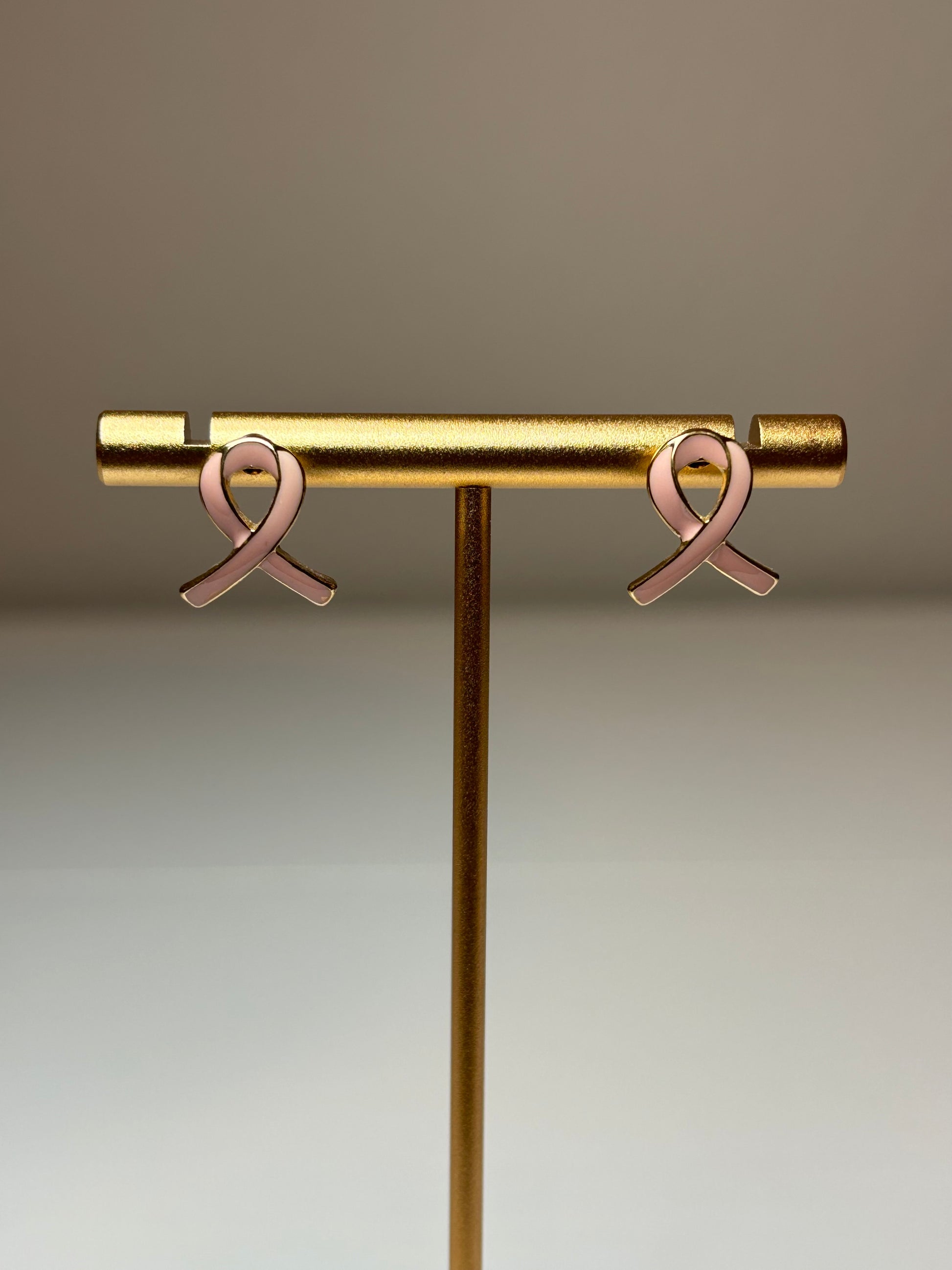 Pink ribbon earrings on a gold background