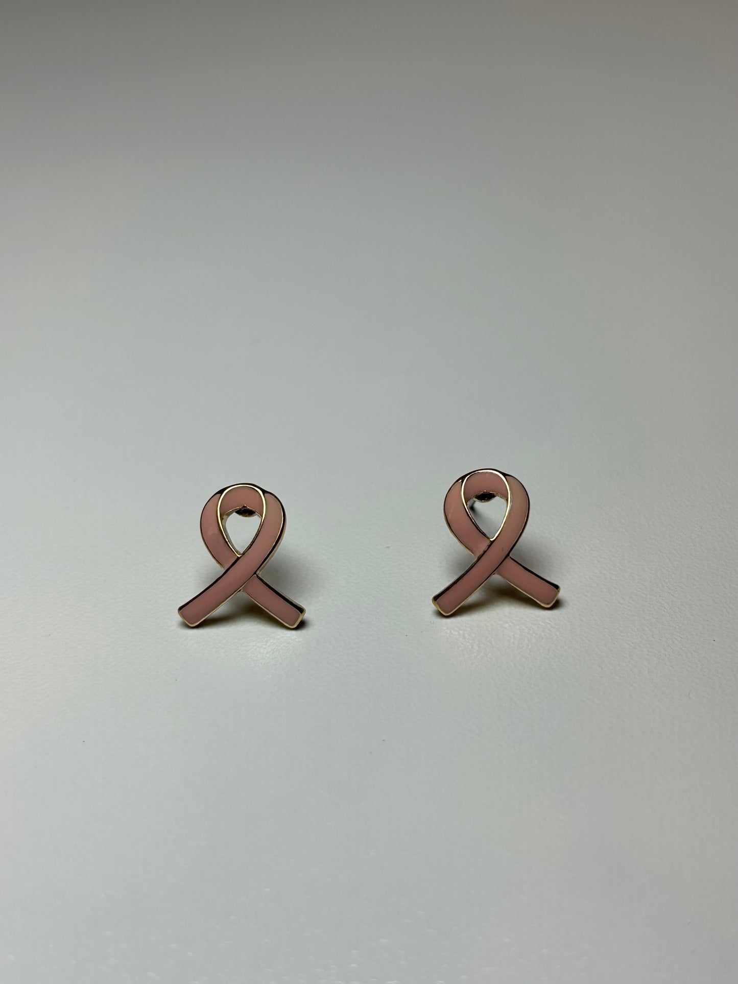 Pink ribbon earrings on a gold background