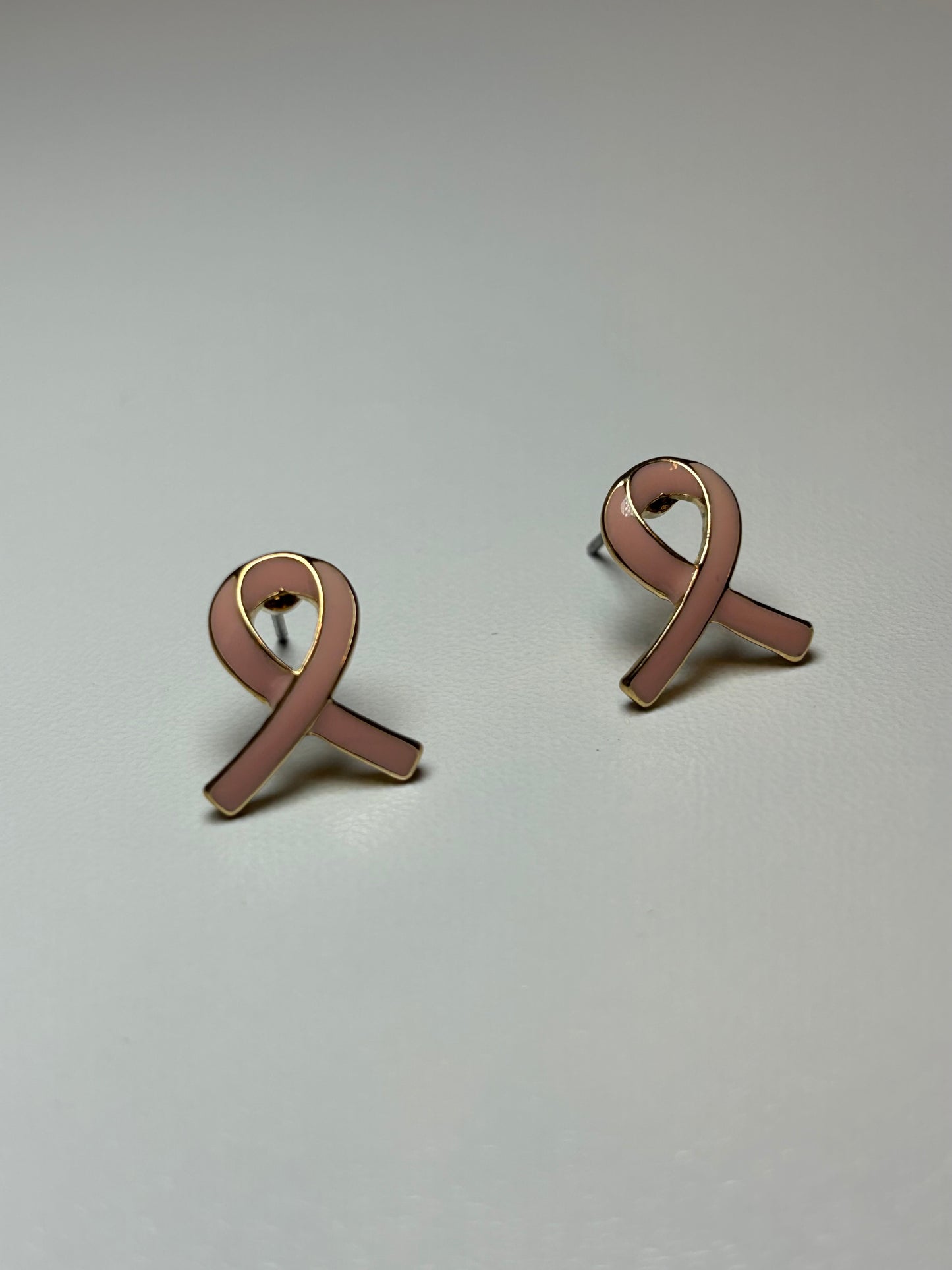 Pink ribbon earrings on a gold background