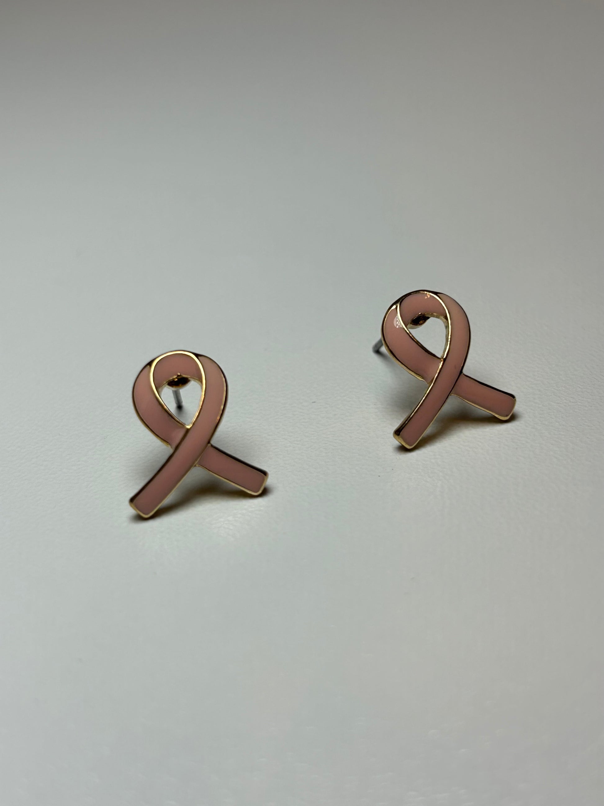 Pink ribbon earrings on a gold background