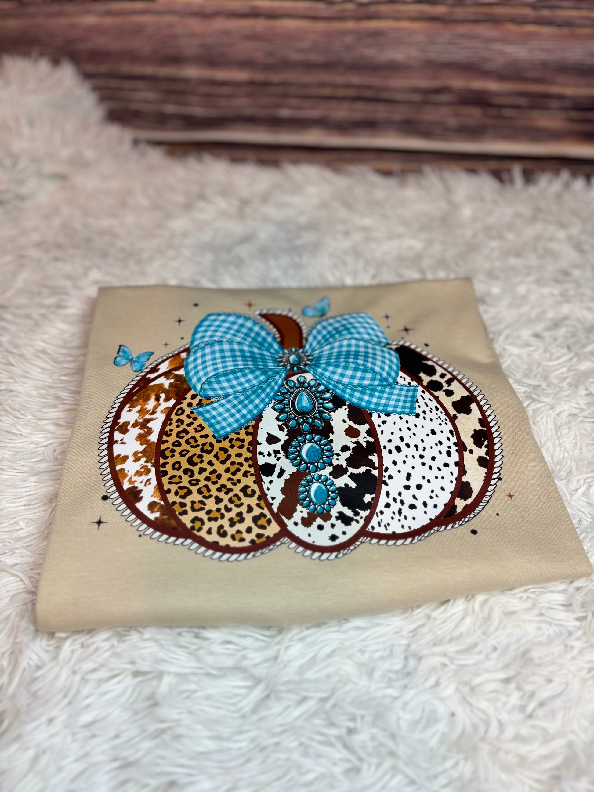 Decorative heat press t-shirt with a western pumpkin that has blue checkered bow, leopard print, and polka dot patterns.