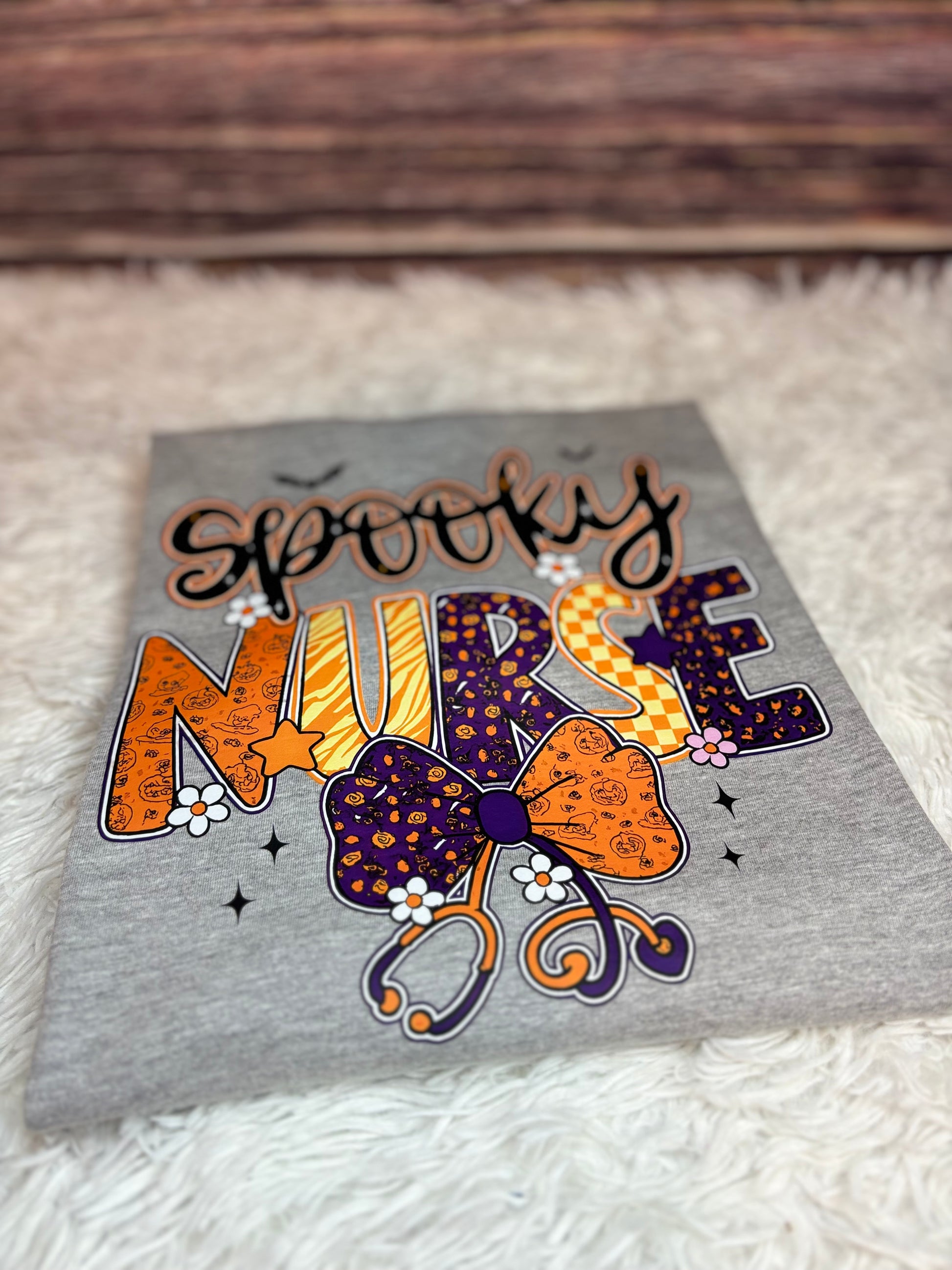 Gray heat press shirt with 'Spooky Nurse' design featuring Halloween elements- bats, stethoscope, flowers, stars
