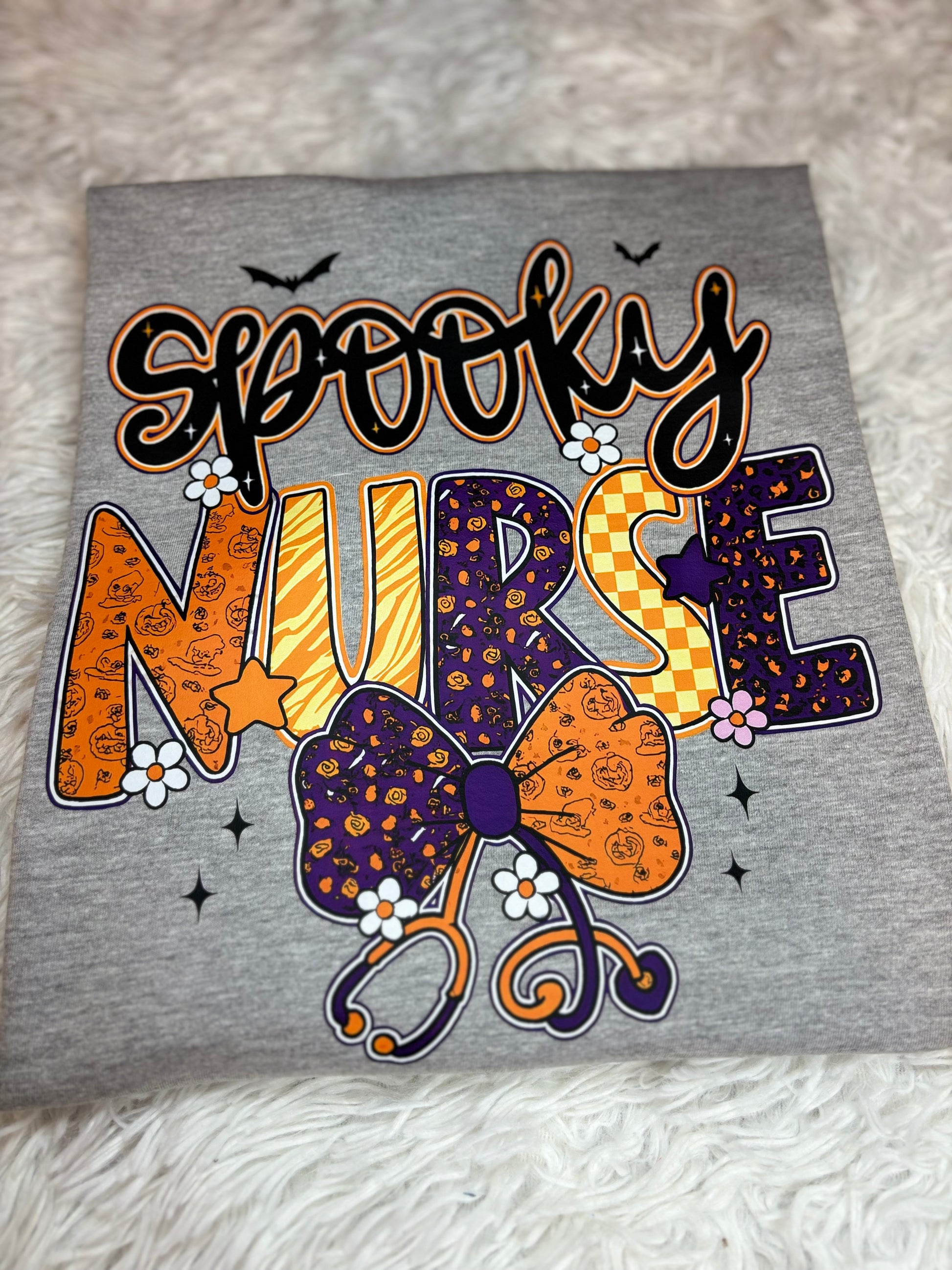 Gray heat press shirt with 'Spooky Nurse' design featuring Halloween elements- bats, stethoscope, flowers, stars