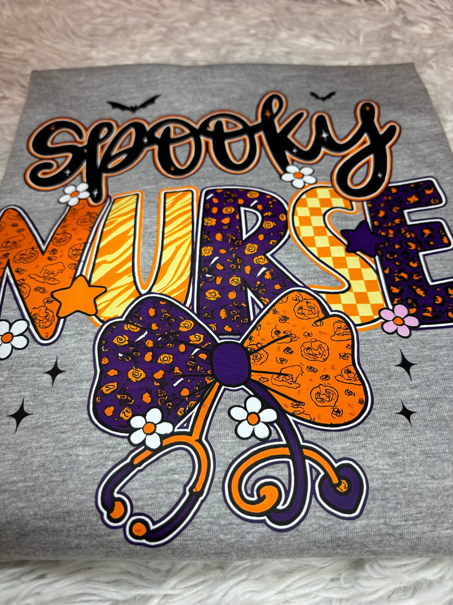 Gray heat press shirt with 'Spooky Nurse' design featuring Halloween elements- bats, stethoscope, flowers, stars