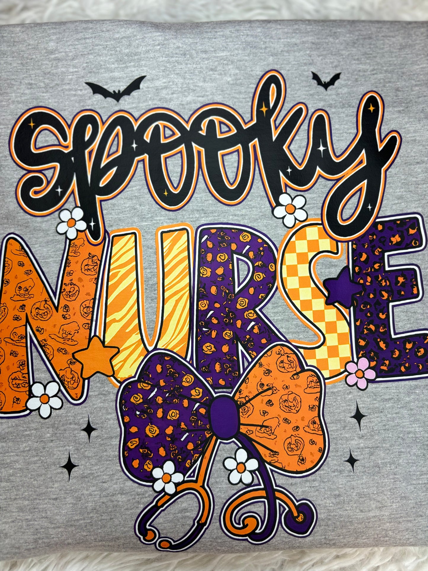 Gray heat press shirt with 'Spooky Nurse' design featuring Halloween elements- bats, stethoscope, flowers, stars