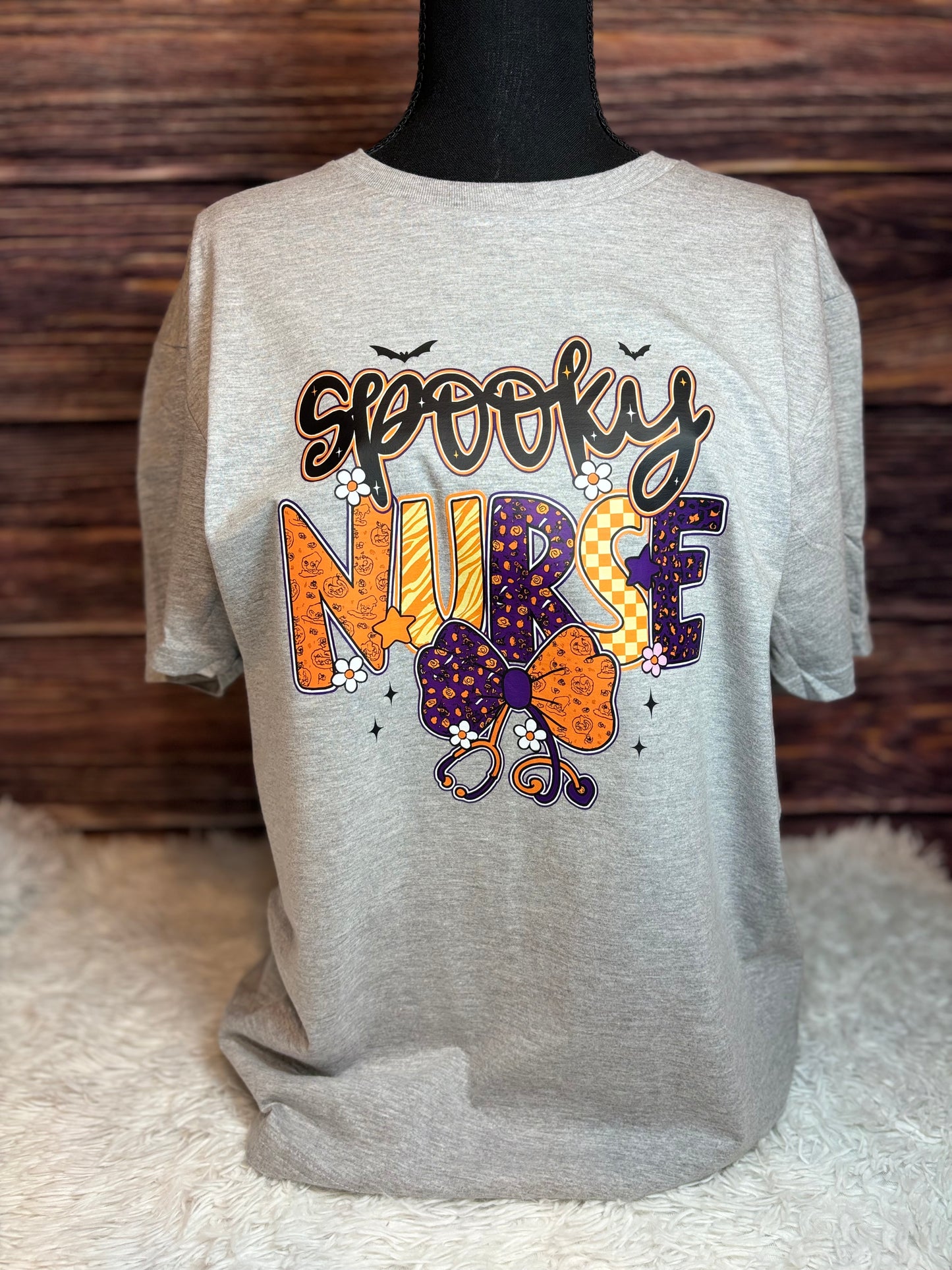 Gray heat press shirt with 'Spooky Nurse' design featuring Halloween elements- bats, stethoscope, flowers, stars