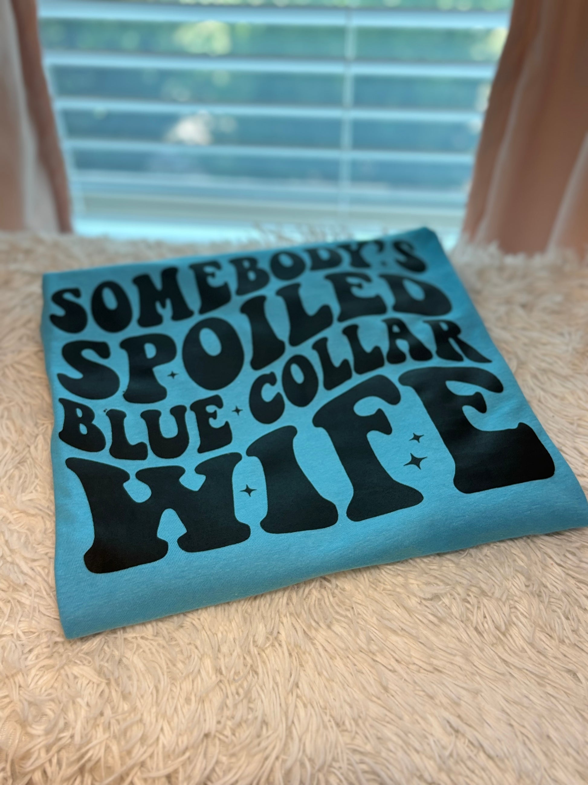 Aqua heat press t-shirt with text 'Somebody's Spoiled Blue Collar Wife' in black 
